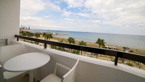 A balcony with a white table and chair, overlooking a beach with palm trees and a marina. - Les Palmiers Boutique Beach Hotel and Luxury Apartments in Larnaca (Cyprus, Larnaca)