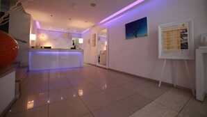 A modern reception area with a reception desk, a large mirror, and a wall-mounted information board. - Les Palmiers Boutique Beach Hotel and Luxury Apartments in Larnaca (Cyprus, Larnaca)