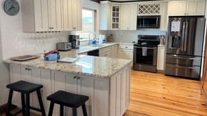 A kitchen with white cabinets, a granite countertop, a stainless steel refrigerator, and a built-in oven. - Anchor's Away- Canal House with Private Dock (Holden Beach)