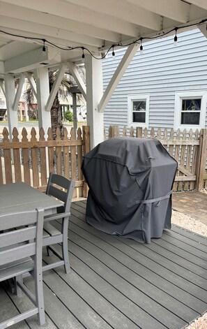 A covered outdoor patio with a table and chairs, a barbecue grill, and a wooden fence. - Anchor's Away- Canal House with Private Dock (Holden Beach)