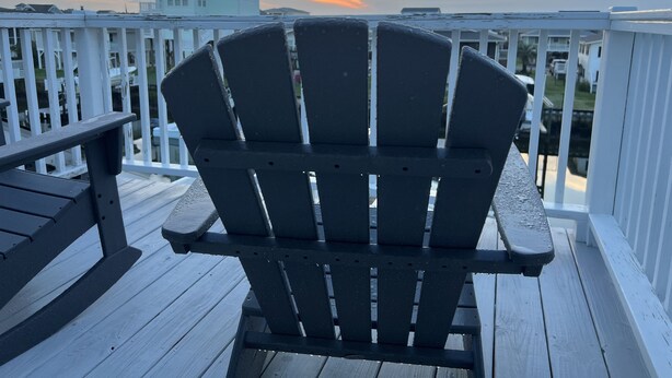 A wooden deck with a black Adirondack chair facing a white railing. - Anchor's Away- Canal House with Private Dock (Holden Beach)