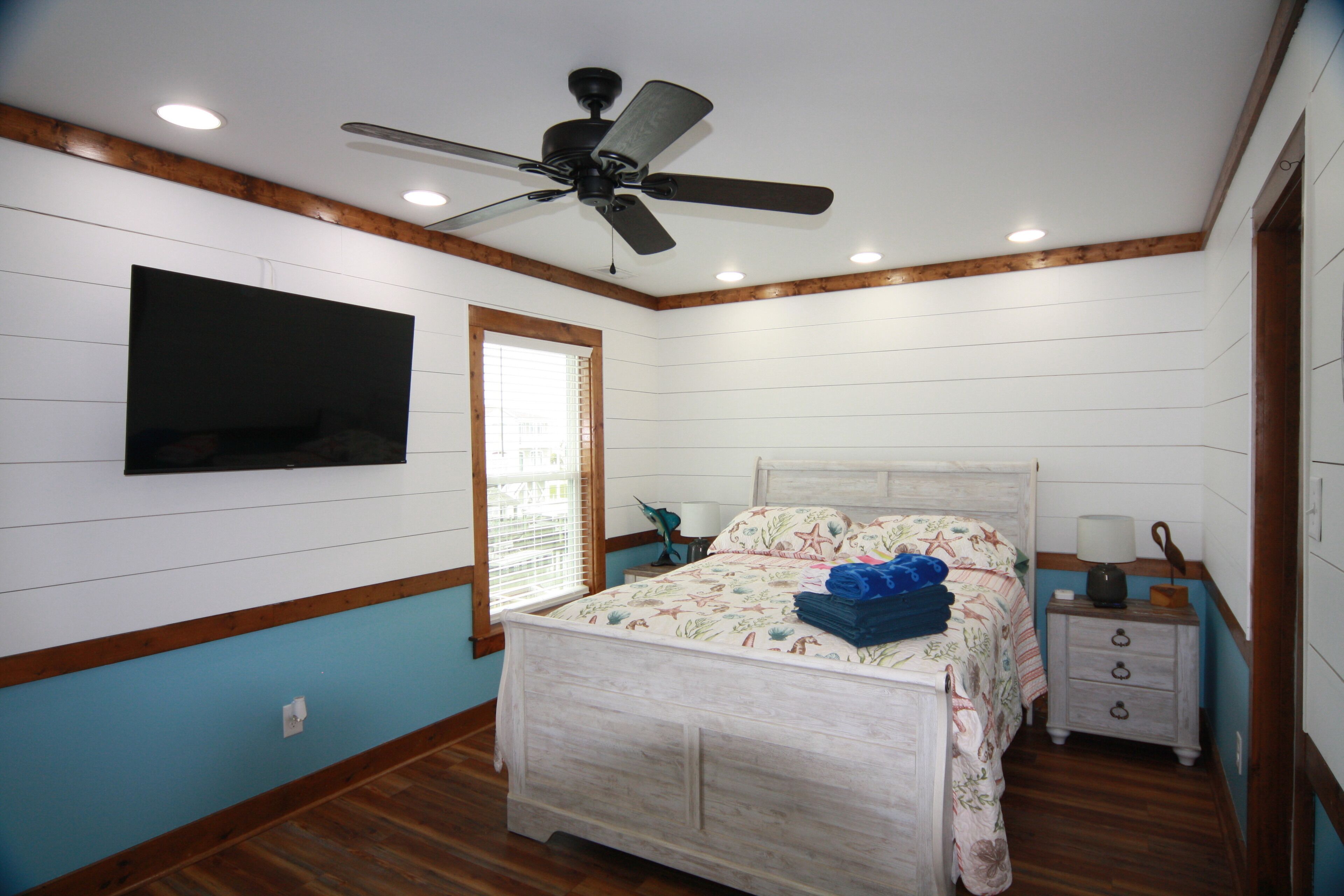 Une chambre à coucher comprenant un lit, une table de chevet, un ventilateur de plafond et un téléviseur fixé au mur.