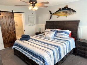 A bedroom with a bed, a nightstand, a dresser, a ceiling fan, and a fish wall art piece. - Anchor's Away- Canal House with Private Dock (Holden Beach)