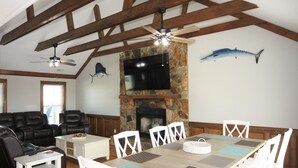 A dining area with a stone fireplace, wooden beams, and a mounted TV. - Anchor's Away- Canal House with Private Dock (Holden Beach)