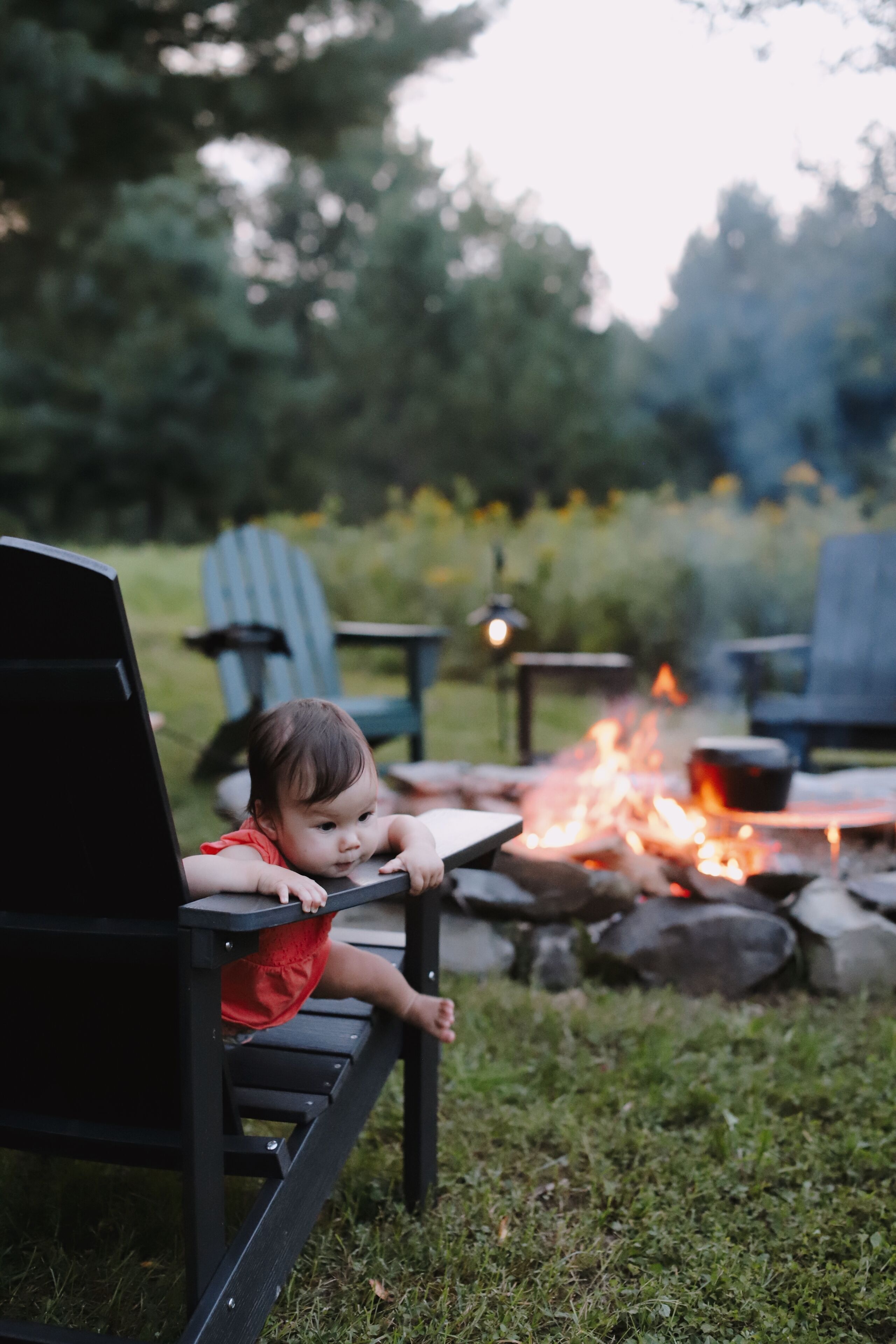 A child sitting on a bench outdoors with a fire in the background.