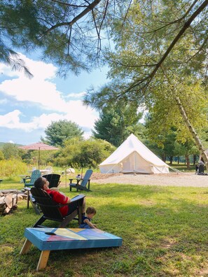 A tented camping area with a dining table and chairs, a child playing on a mat, and a person relaxing on a chair. - Private Glamping Site at Family-Run Farm, Blind Buck Valley Farmstead (Salem)