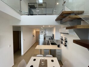 Eine moderne Küche mit einer zentralen Kochinsel, einem Essbereich mit Glastisch und einer Treppe, die zwei Etagen verbindet.