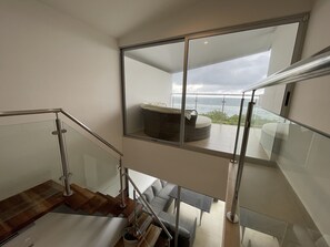 Ein modernes Interieur mit einer Glasstiege, einer Sitzecke mit Meerblick und einem Balkon mit Korbstuhl.