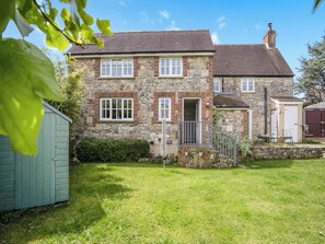 A stone house with a front porch, a small garden, and a shed.