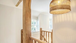 En trätrappa med en flätad lampa, vita väggar och fönster med persienner.