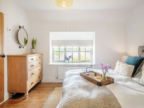A bedroom with a wooden dresser, a radiator, a window with a view, and a bedside table with a tray.
