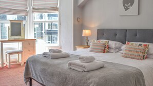 Ein ordentlich bezogenes Bett mit gefalteten Handtüchern, ein Schreibtisch mit Stuhl und ein Fenster mit Jalousien.