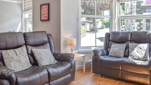 Ein Zimmer mit zwei Ledersofas, einem kleinen Tisch und einem Fenster mit Blick auf eine Straße und Gebäude.
