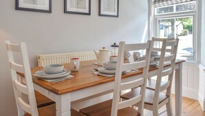 Ein Essbereich mit Holztisch, gedecktem für vier Personen, weißen Stühlen und gerahmten Pflanzenbildern an der Wand.