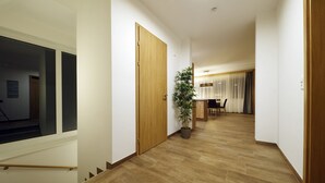 A hallway with wooden flooring, a potted plant, a wooden door, and a view into a room with a dining table and chairs.