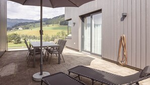 A patio with a table and chairs, a lounge chair, and a view of a green landscape.