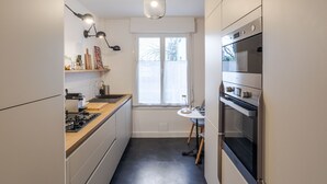 Una cocina compacta con electrodomésticos modernos, una ventana y una lámpara colgante.