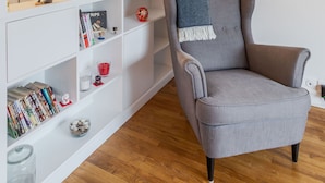 Una habitación con un sillón gris, una estantería blanca con diversos objetos y un espejo grande.