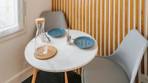 Una habitación con pared de madera a rayas, un cuadro enmarcado, una mesa redonda con una esfera de arena de vidrio, platos azules y una silla gris.