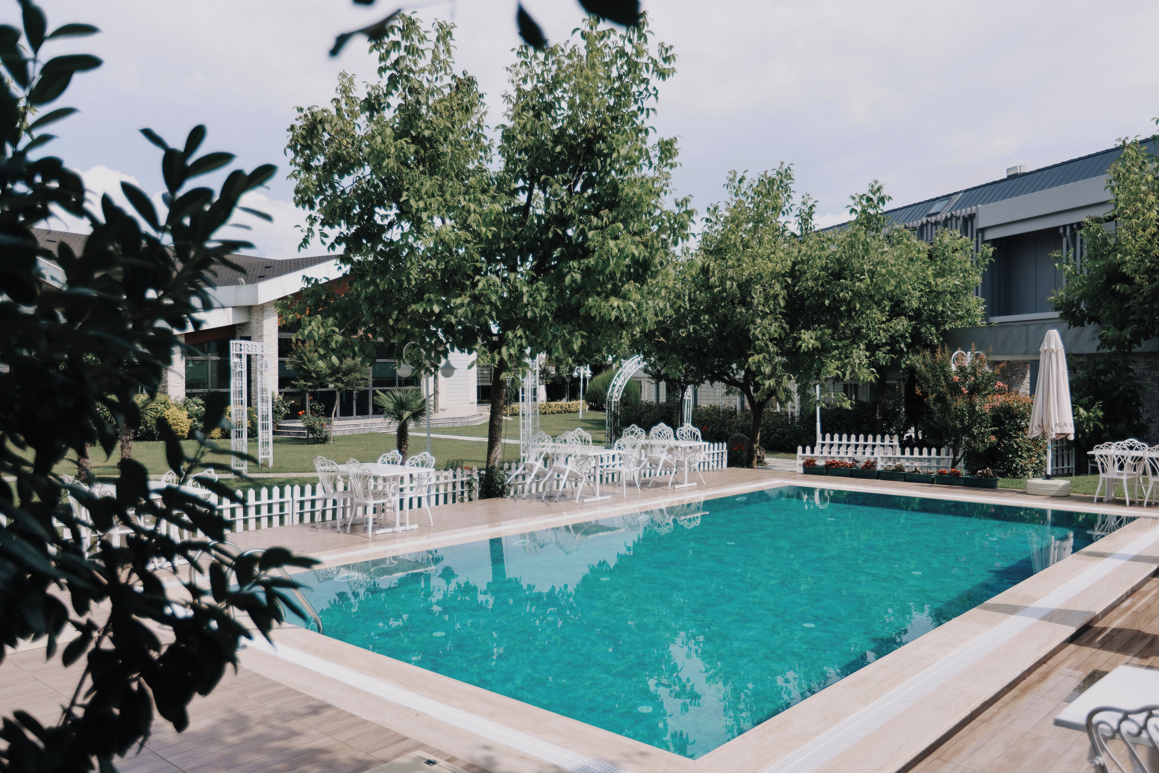 Una piscina rectangular con borde de baldosas, rodeada de sillas blancas y una cerca de piquetes blancos.