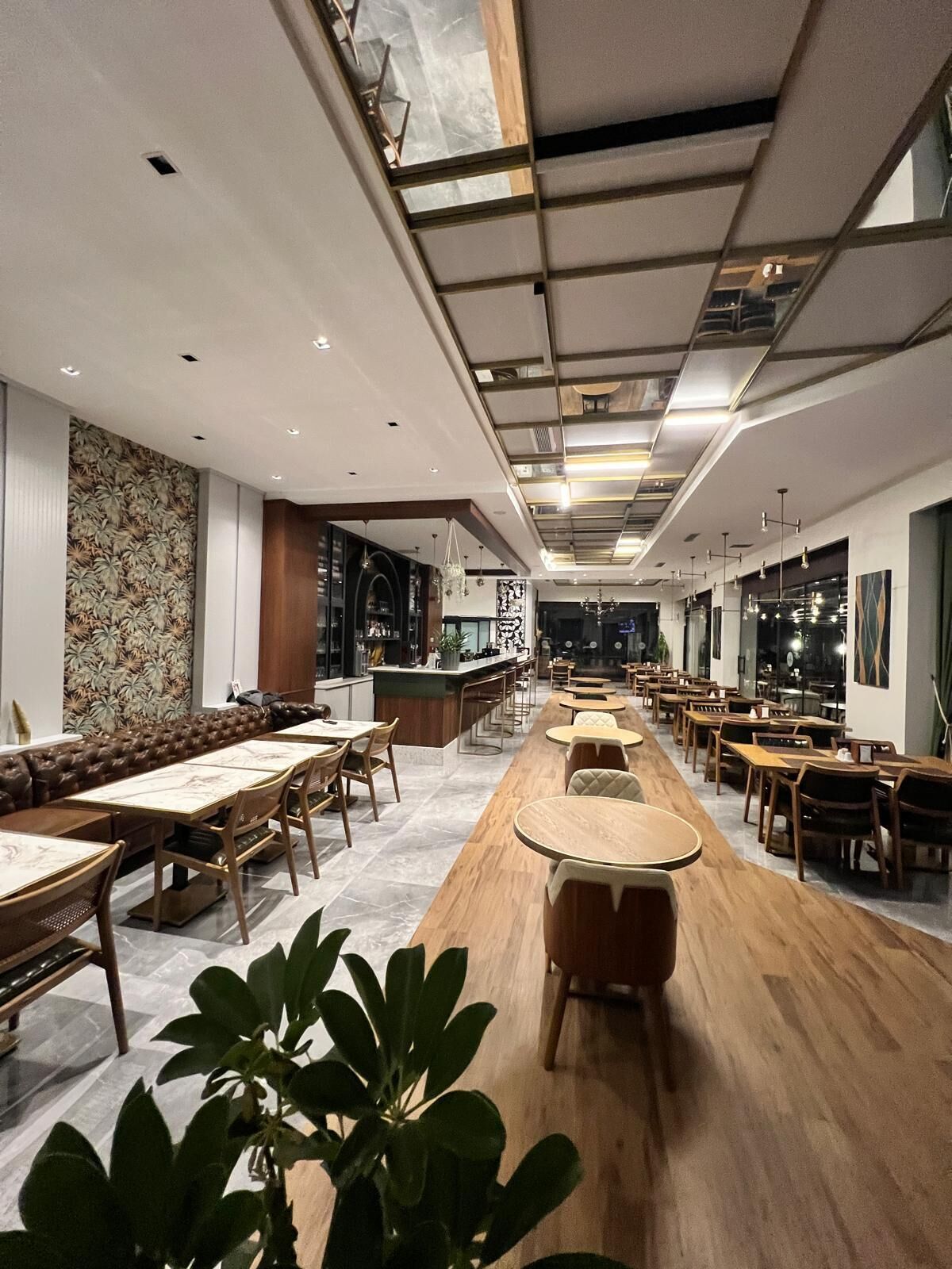 Ein modernes Restaurant mit einer langen Theke, Holztischen und einer Wand mit Muster.
