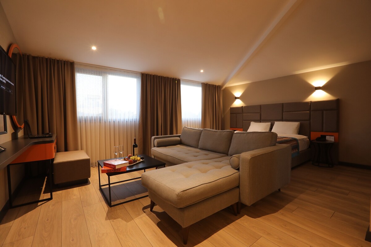 Una habitación de hotel moderna con sofá, una mesita con fruteros, un escritorio y una cama con cabecera.