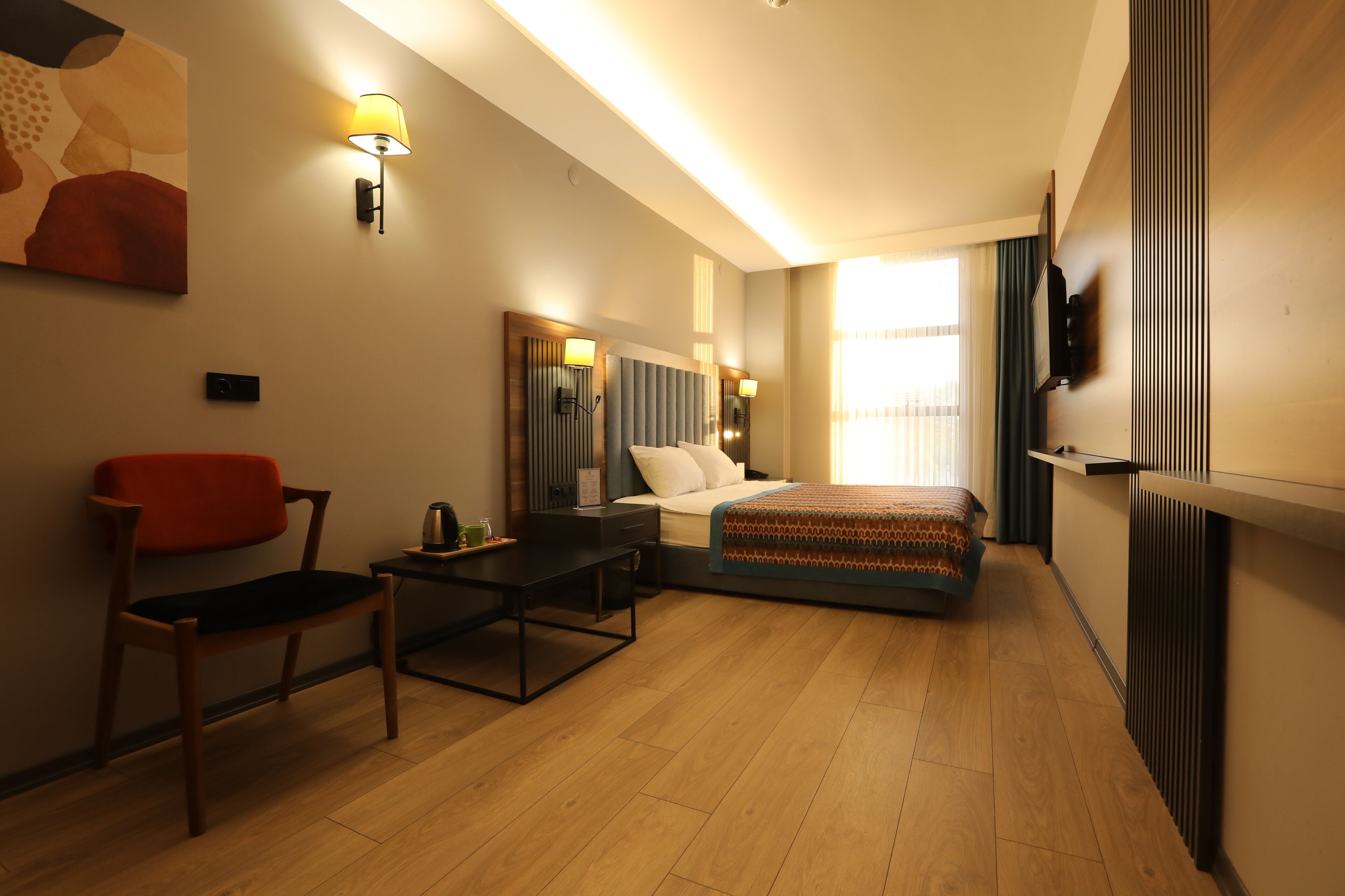 Habitación de hotel con cama, escritorio, silla, televisor y un cuadro en la pared.