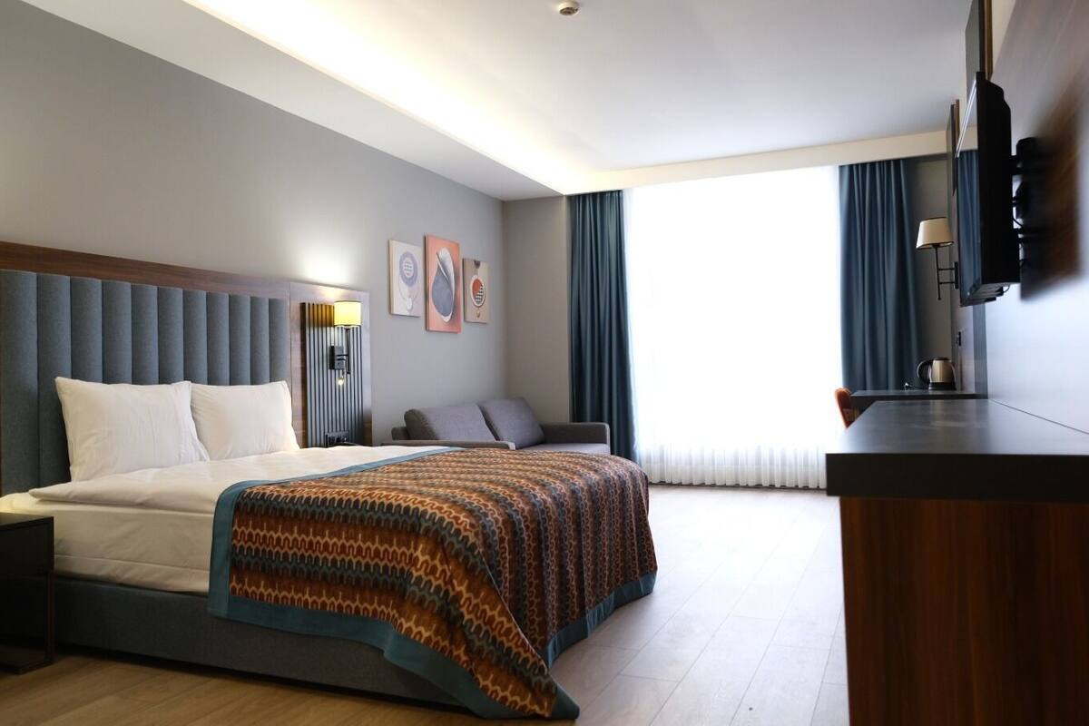 A modern hotel room with a large bed, a desk, and a TV.