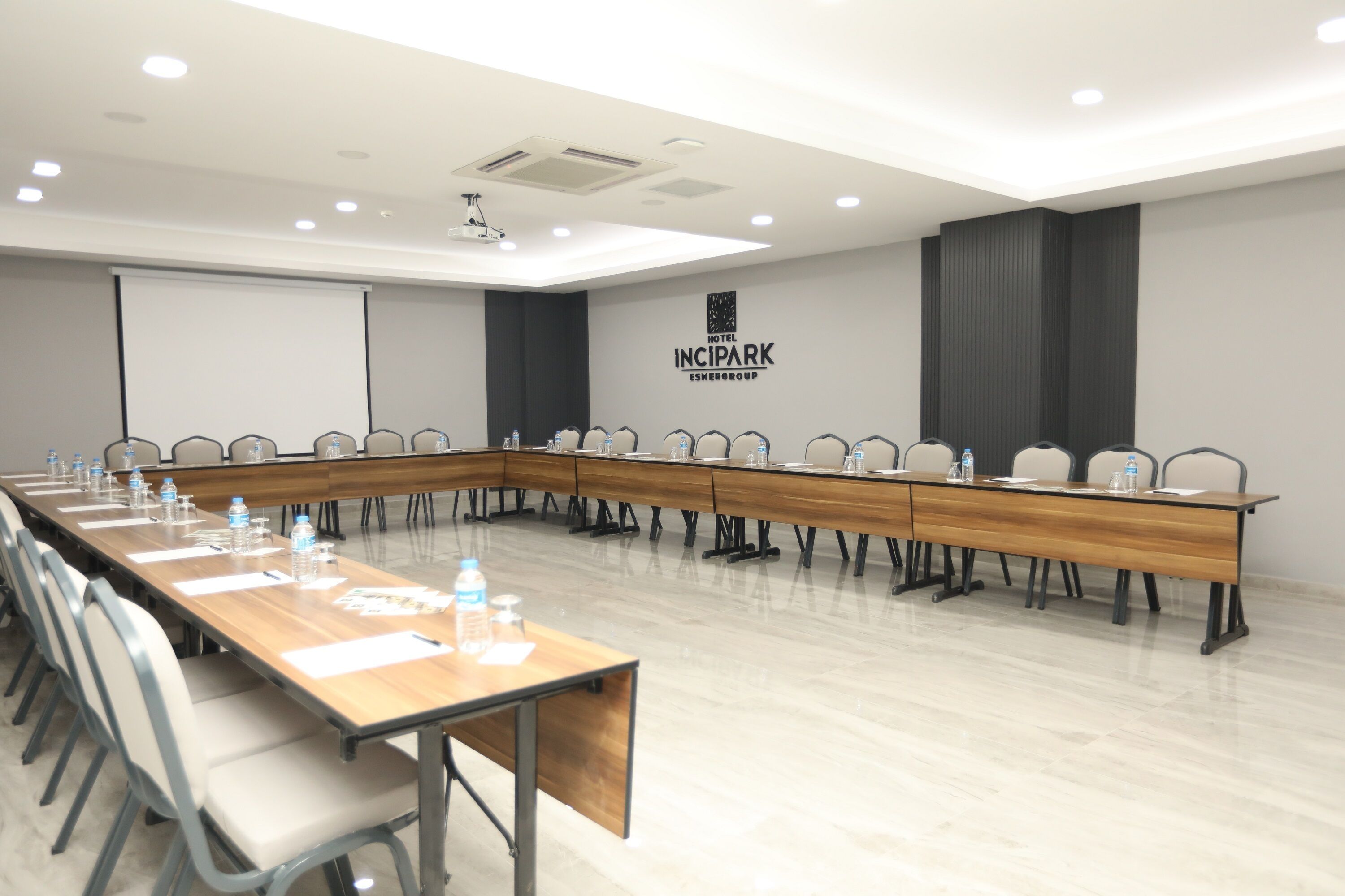 Una sala de conferències amb una taula llarga, cadires, ampolles d'aigua i una pantalla projectora.