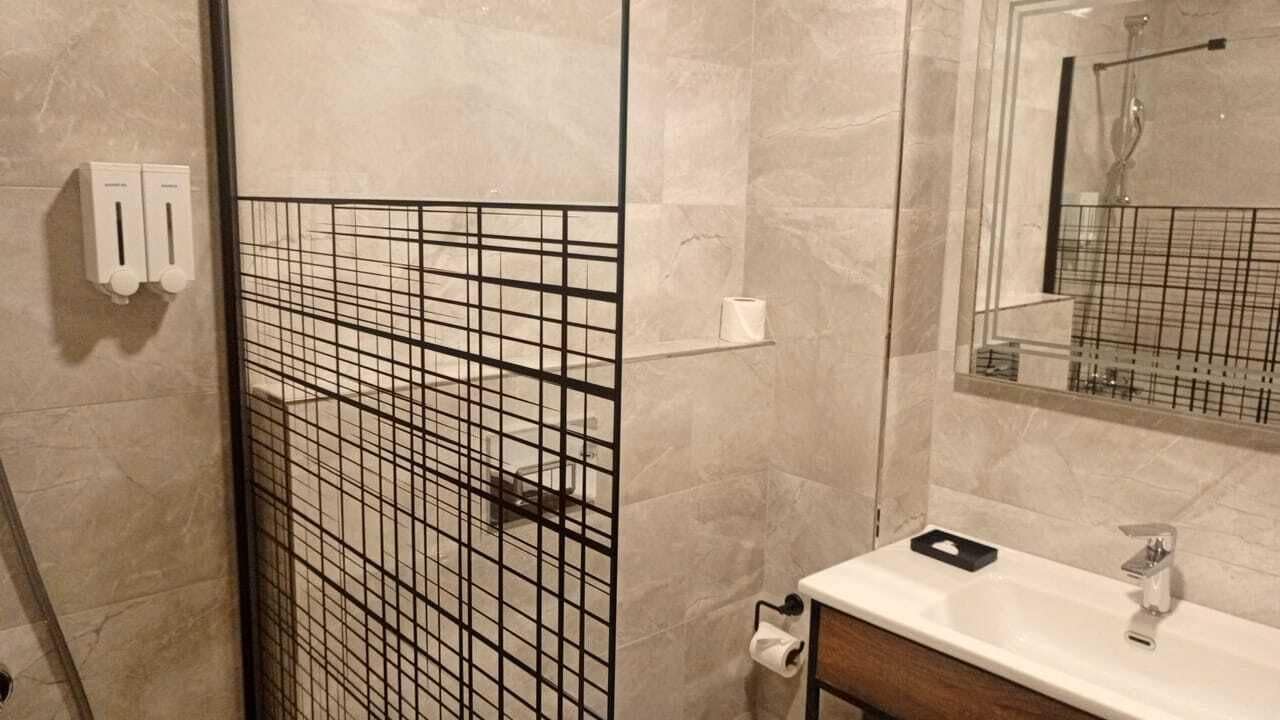 Un baño con cabina de ducha azulejada, un lavabo con espejo y un inodoro.