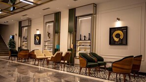 Un vestíbulo de hotel con un piso de mármol pulido, una escalera y zonas de estar con sillas y un sofá.
