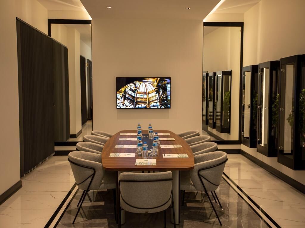 A conference room with a long table, eight chairs, and a large painting on the wall.