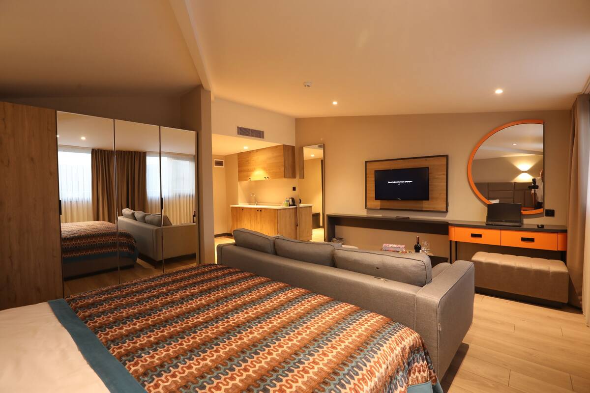 A hotel room with a large bed, a sofa, a TV, a desk, and a mirror.