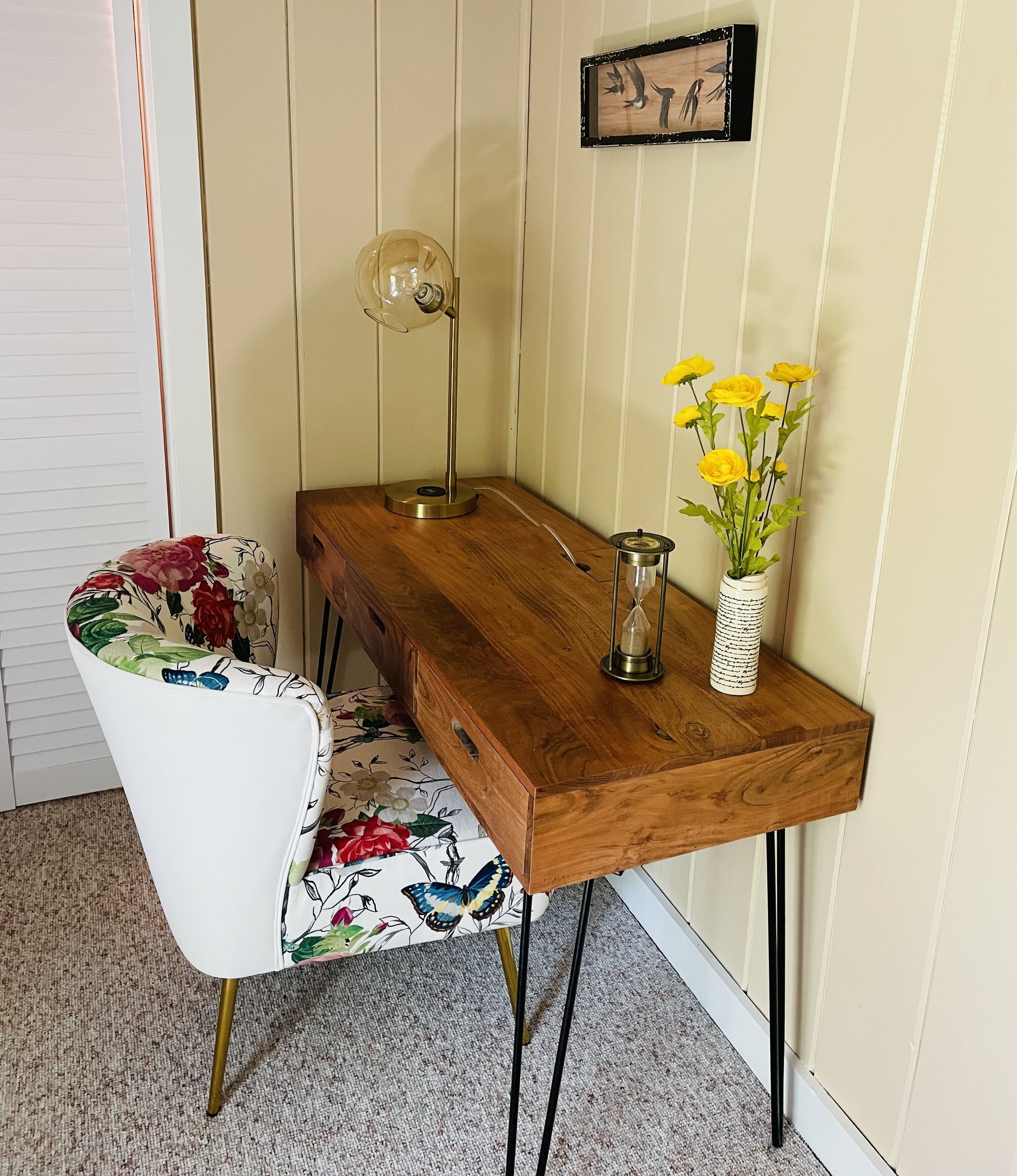 A wooden dining table with a vase of yellow flowers and an hourglass.