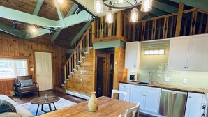 Una cocina amplia con una mesa de comedor de madera, sillas blancas y un lavavajillas de acero inoxidable.