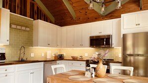 Una cocina moderna con armarios blancos, una mesa de comedor de madera y un refrigerador de acero inoxidable.