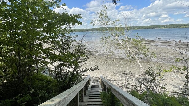 Una escalera de madera que lleva a una playa, con vista al agua y a la costa distante.
