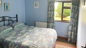 Een slaapkamer met een bed, een radiator, een raam met gordijnen en ingelijste foto’s aan de muur.