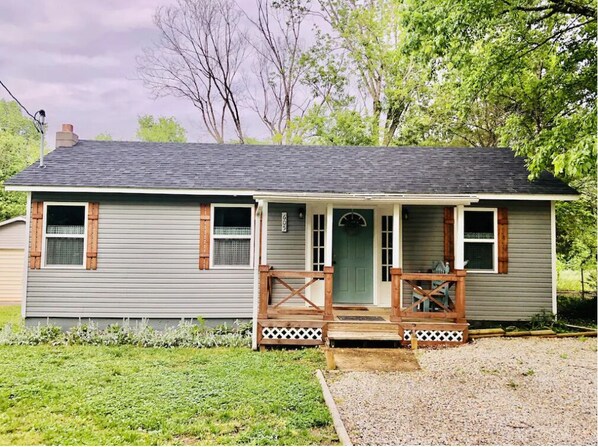 A single-story house with a front porch, a green door, and a gravel driveway.