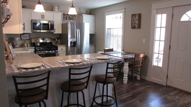 A modern kitchen with stainless steel appliances, a central island with bar stools, and a dining area with a view of the outdoors.