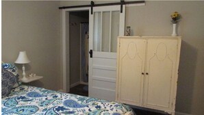 Een slaapkamer met een bed, nachtkastje, kaptafel en een deur naar een gang.