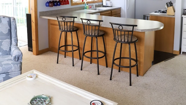 A compact kitchen with a central island, wooden cabinets, and a dining area with bar stools. - Vacation Home at Point Sebago Resort (Casco)