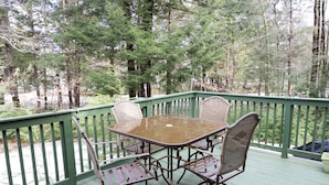 A wooden deck with a table and chairs, surrounded by a green railing, overlooking a forested area. - Vacation Home at Point Sebago Resort (Casco)