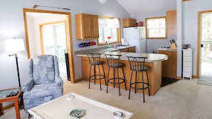 A compact kitchen with wooden cabinets, a central island with bar stools, a refrigerator, and a coffee maker. - Vacation Home at Point Sebago Resort (Casco)