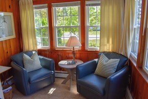 Une pièce chaleureuse avec deux fauteuils en cuir bleu, une petite table avec une lampe et de grandes fenêtres avec des rideaux.