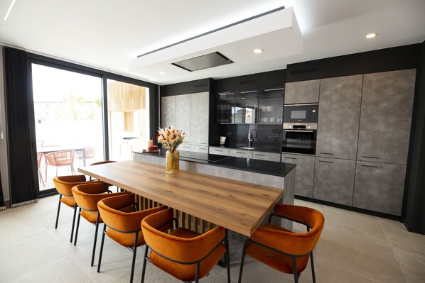 A modern kitchen with a wooden island, black cabinets, and orange chairs.