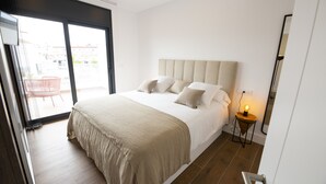 Moderni hotellihuone, jossa on suuri sänky, yöpöytä lampun kanssa ja näkymä ulkoalueelle liukuoven kautta.