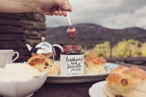 A rustic table setting with scones, a jam jar, and a teapot.