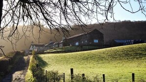 Ländliche Landschaft mit einem Steinhaus, einem Feldweg und einem grasbewachsenen Hügel.