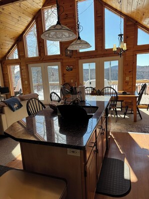 Interior d'una cabana acollidora amb una gran illa de cuina, parets de fusta i finestrals que donen vista a un paisatge nevà.